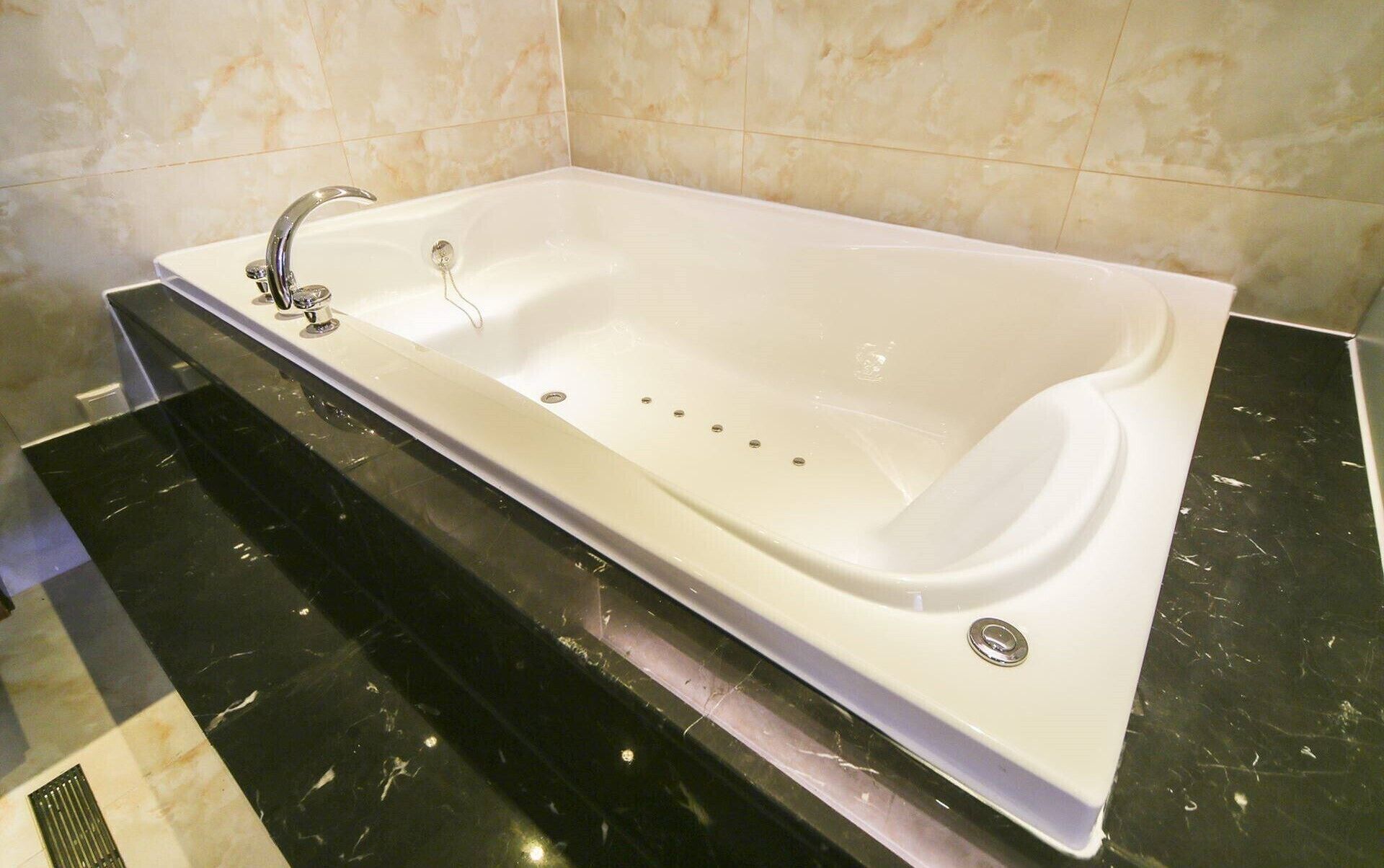 A rectangular bathtub with a single faucet, set against a tiled wall and a black countertop.