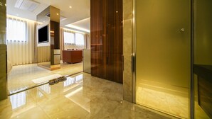 Une chambre d’hôtel moderne dotée d’un grand miroir, d’un téléviseur à écran plat, d’une armoire en bois et d’une porte en verre.