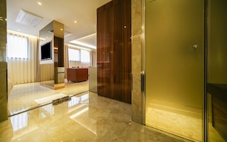 A modern hotel room with a large mirror, a flat-screen TV, a wooden wardrobe, and a glass door.