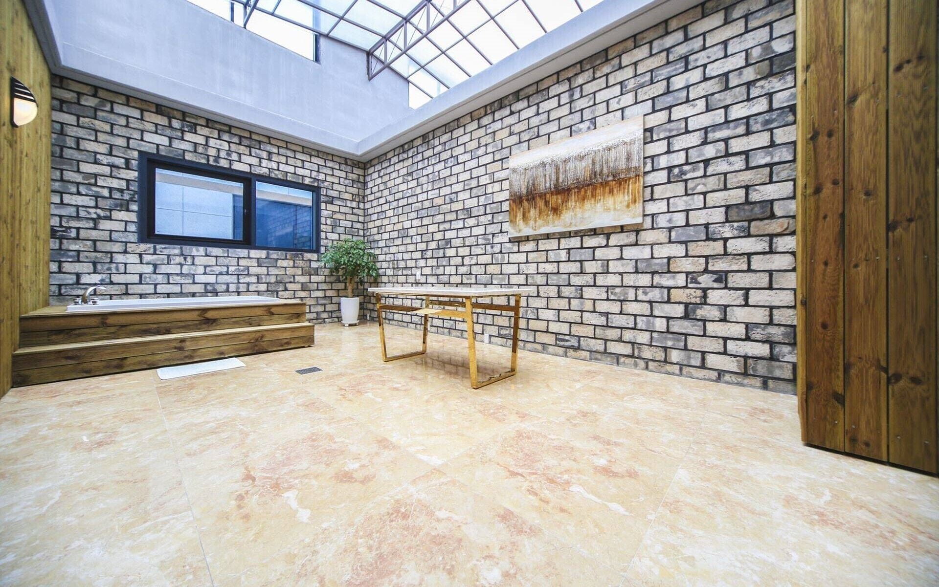 A room with a brick wall, a large window, a wooden bench, a small table, and a plant.
