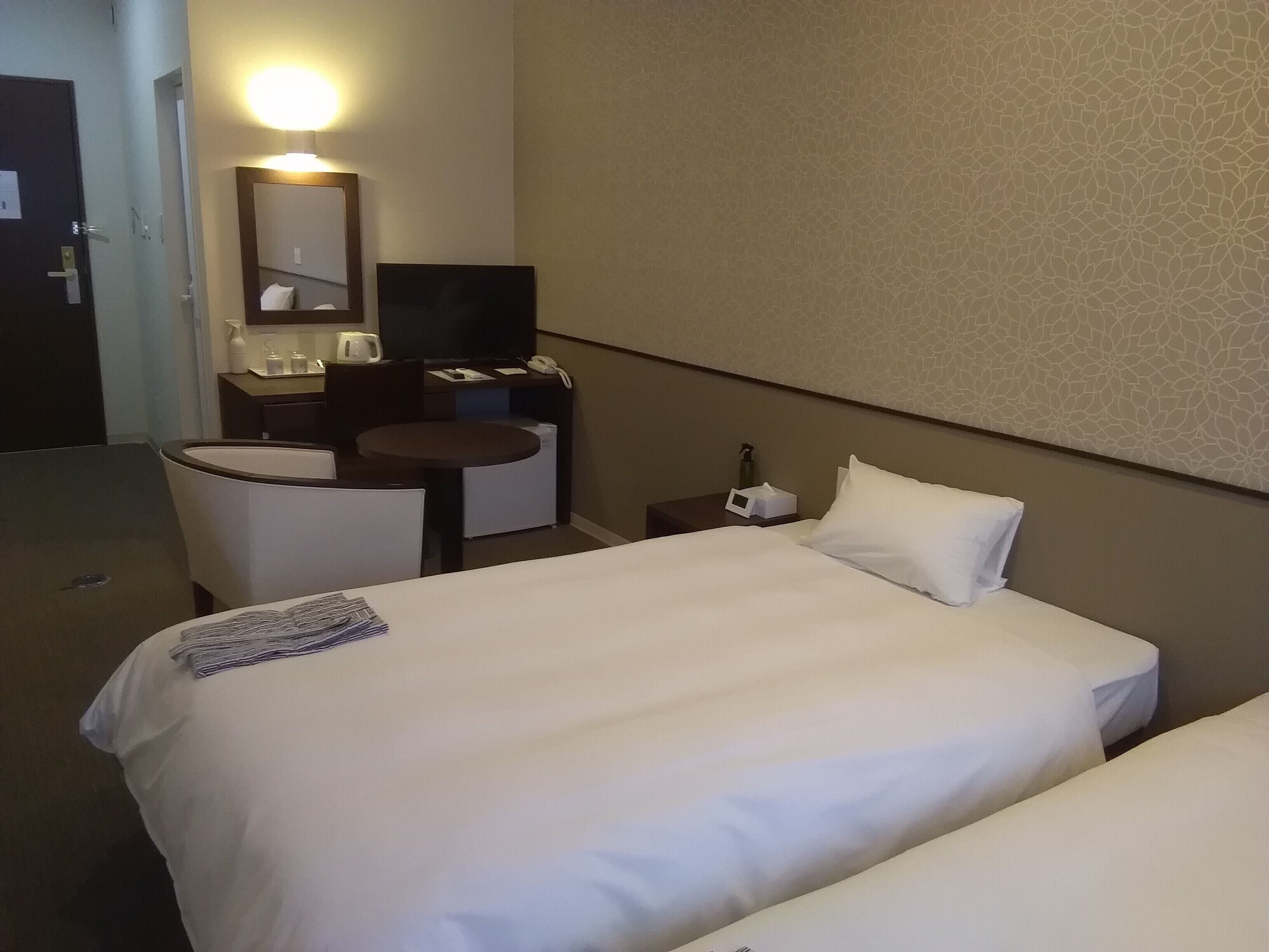Une chambre d’hôtel avec deux lits, un bureau, une chaise, une petite table, un téléviseur et un miroir.