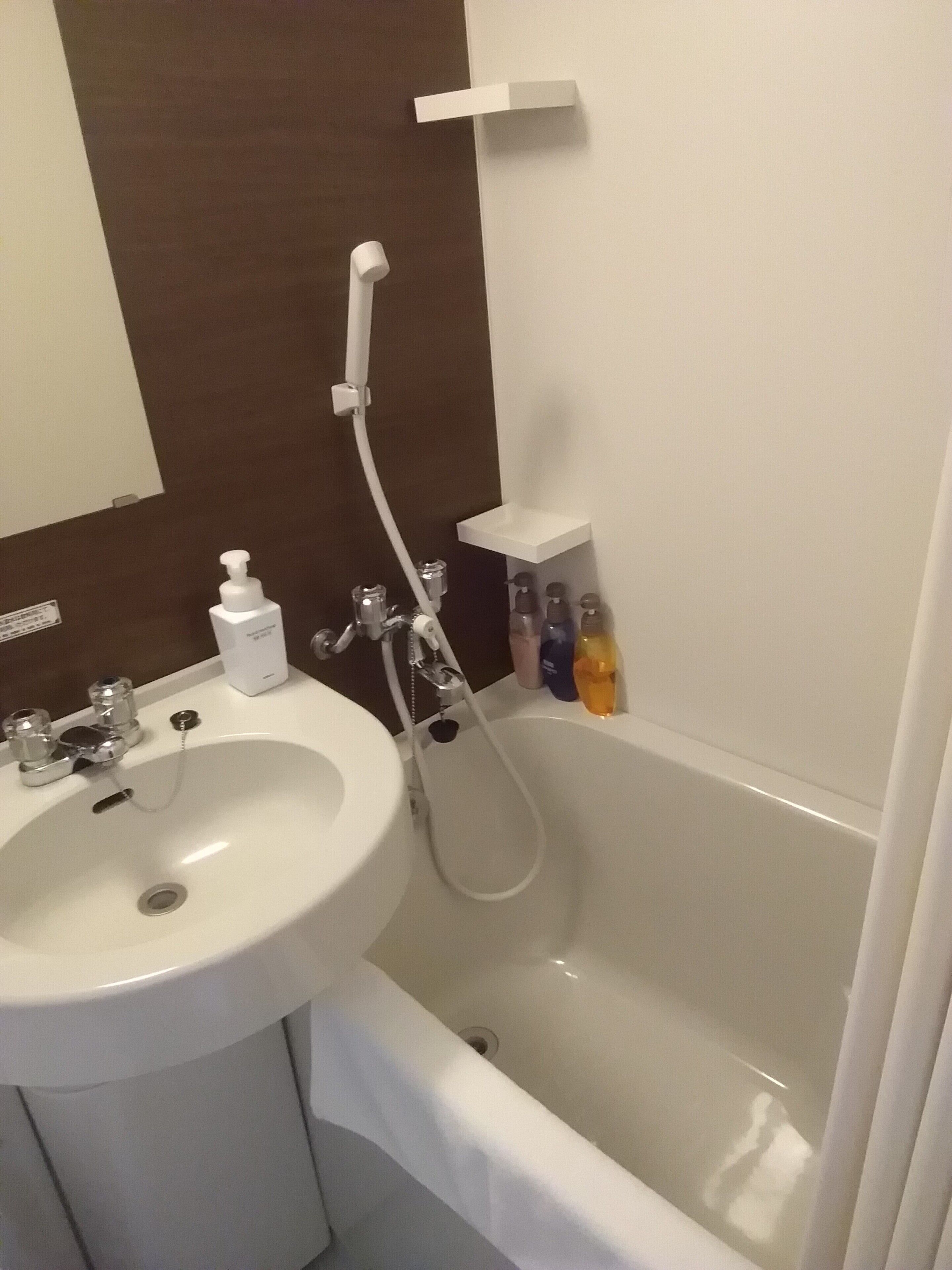 Ein Badezimmer mit weißem Waschbecken, einer Badewanne und einer Dusche. An der Wand befinden sich Pflegeprodukte.