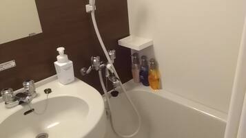 Ein Badezimmer mit weißem Waschbecken, einer Badewanne und einer Dusche. An der Wand befinden sich Pflegeprodukte.