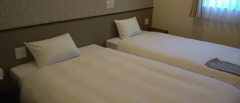 Dos camas individuales con ropa de cama blanca en una habitación de hotel.