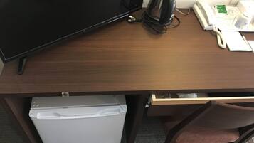 Un escritorio de madera con un televisor de pantalla plana, una tetera eléctrica negra, un teléfono blanco y un pequeño electrodoméstico blanco.