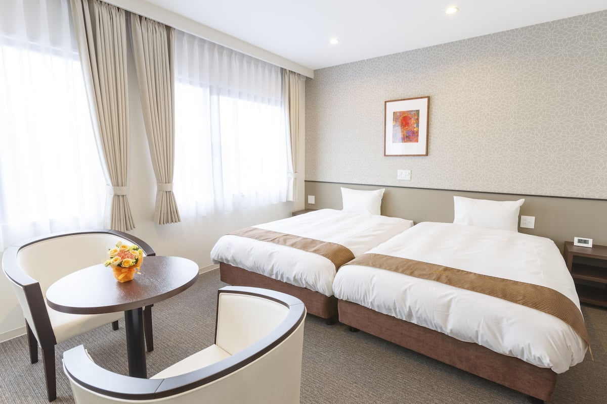 Ein Hotelzimmer mit zwei Betten, einem kleinen Tisch mit Blumenvase und einem Sessel.