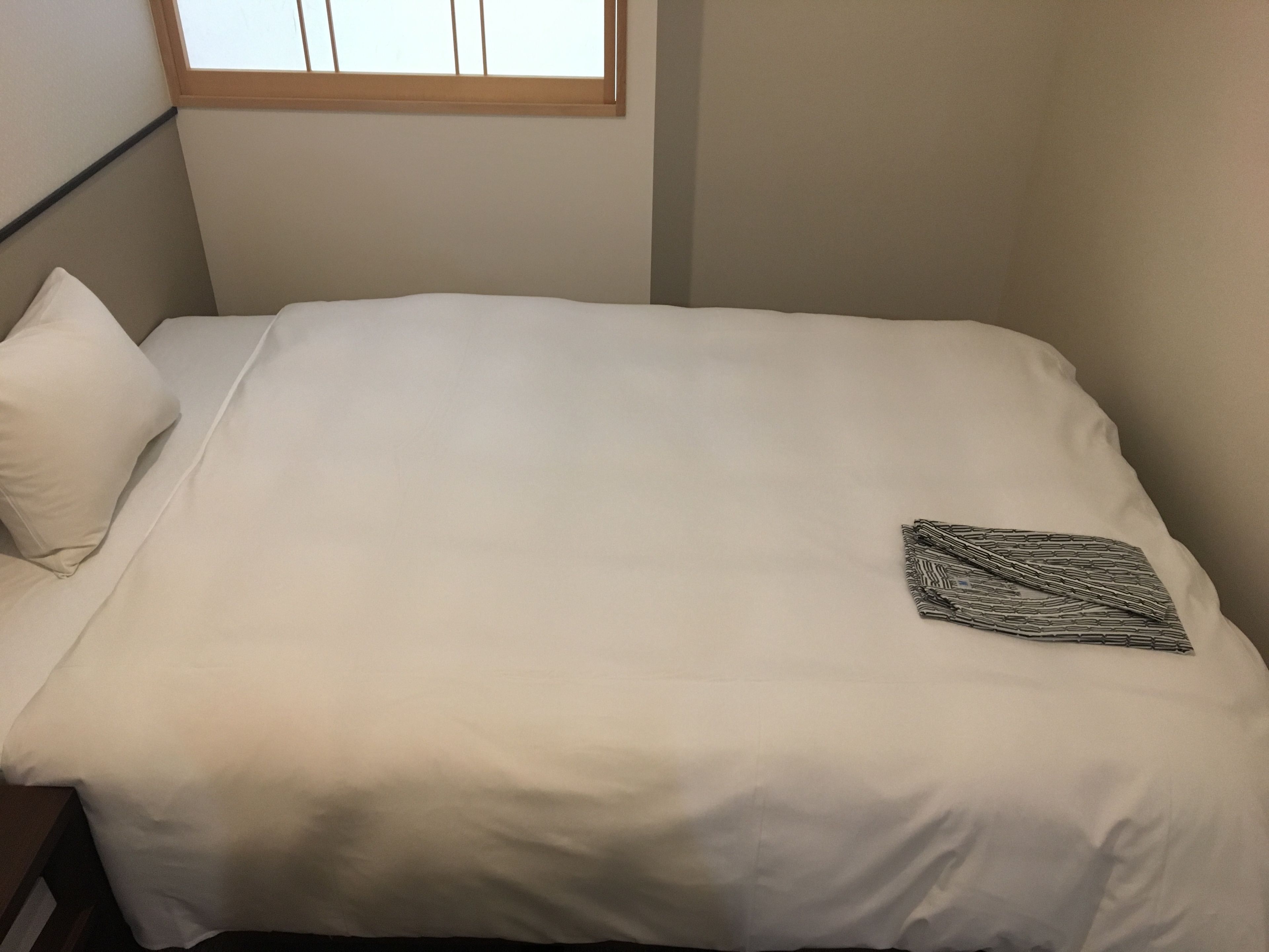 A small, neatly made bed with white linens and a single patterned pillow.