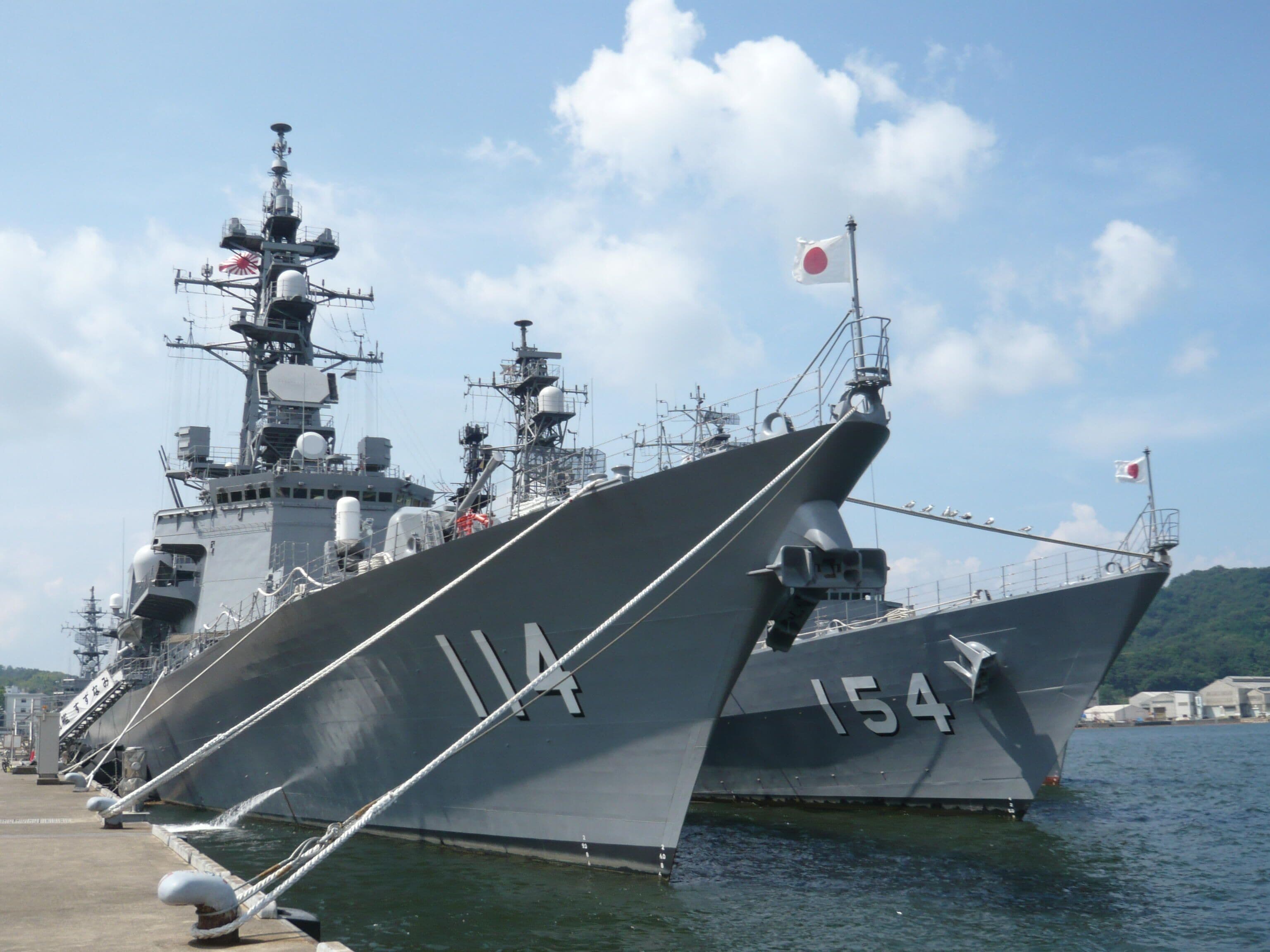 A large naval ship docked at a port with visible identification numbers and flags.