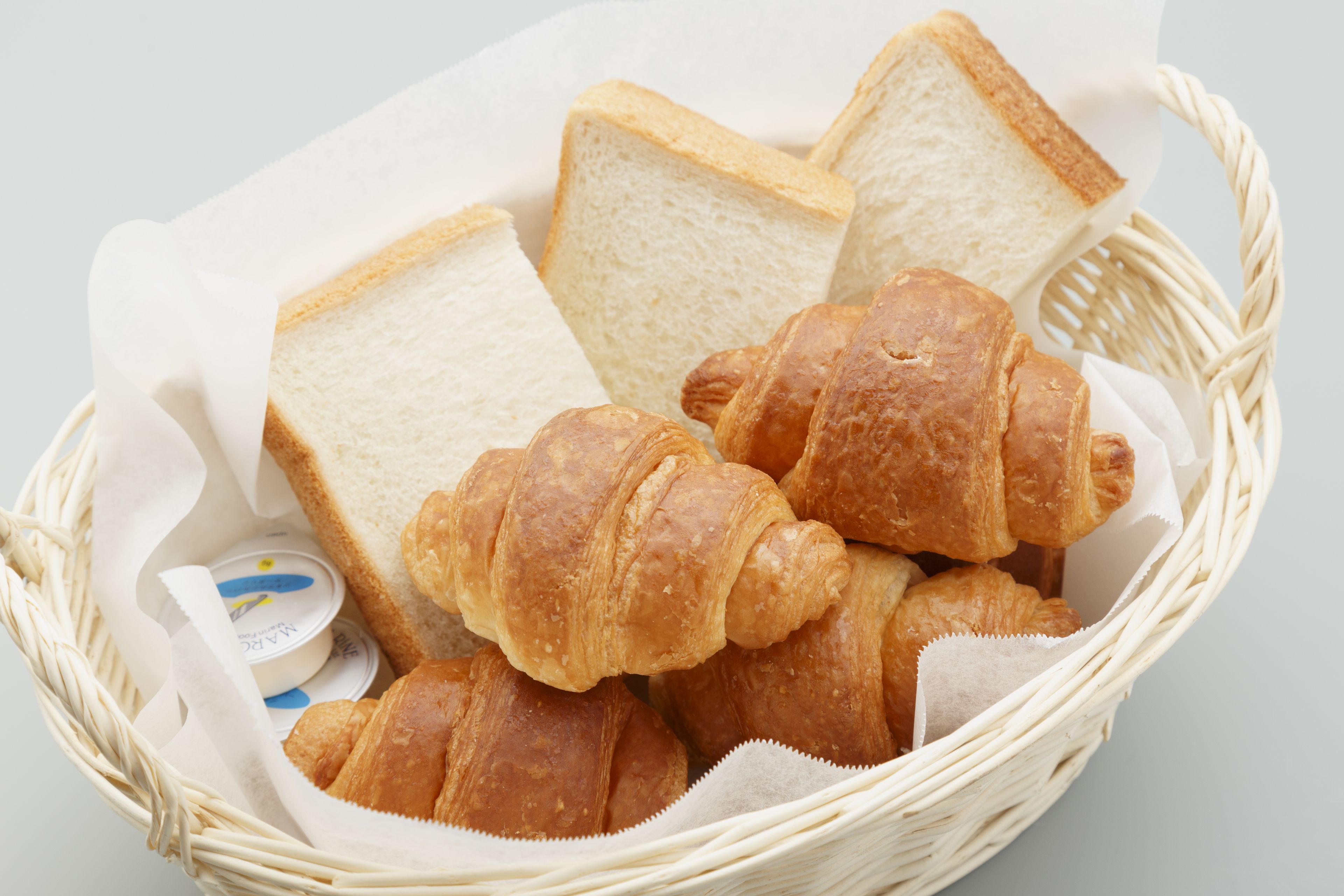 A basket containing several croissants and slices of white bread.