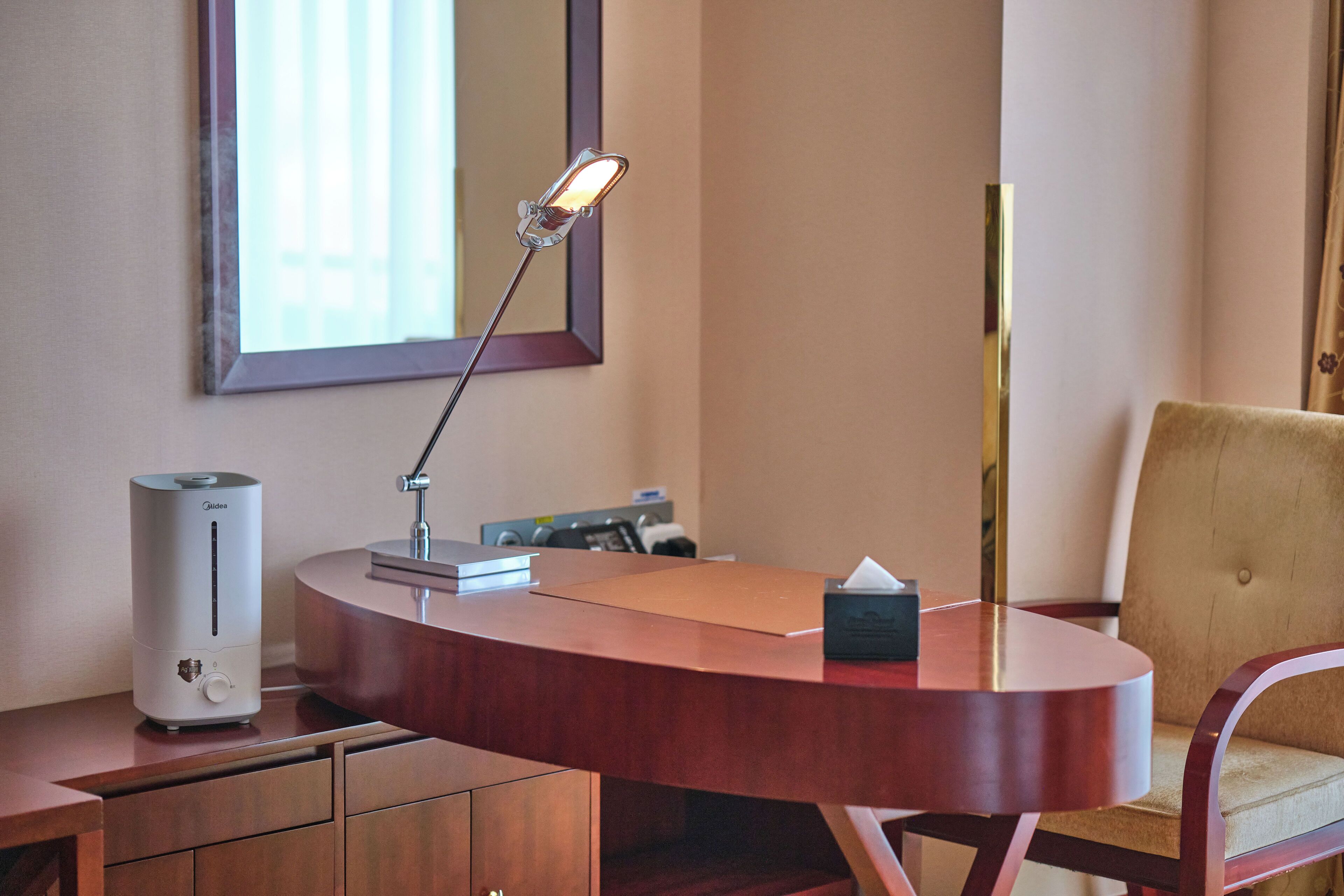 Een hotelkamer met een bureau, een lamp, een stoel, een nachtkastje en een bed.