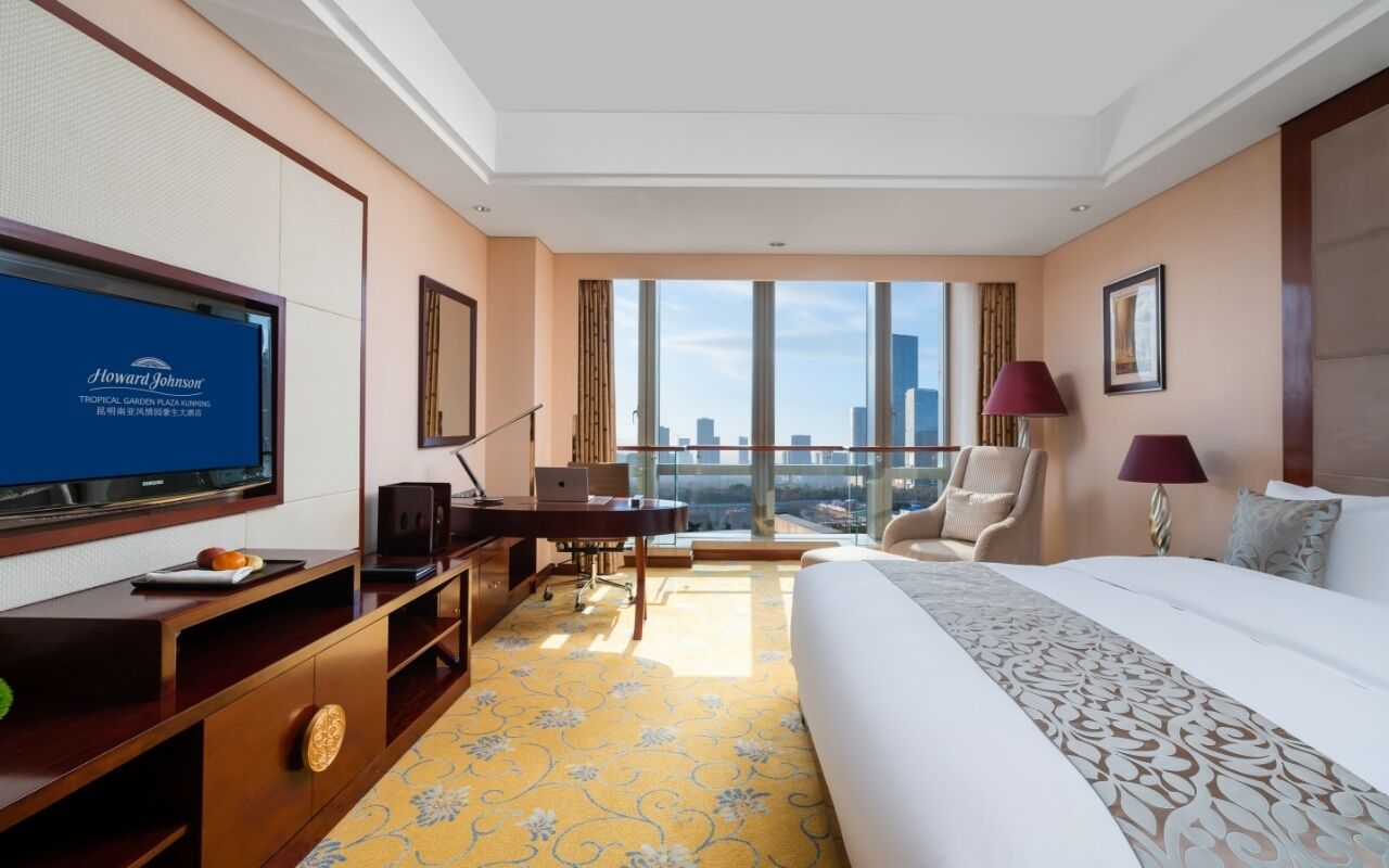 Una habitació d'hotel amb un llit gran, una taula de treball, una televisió i vista a la ciutat.
