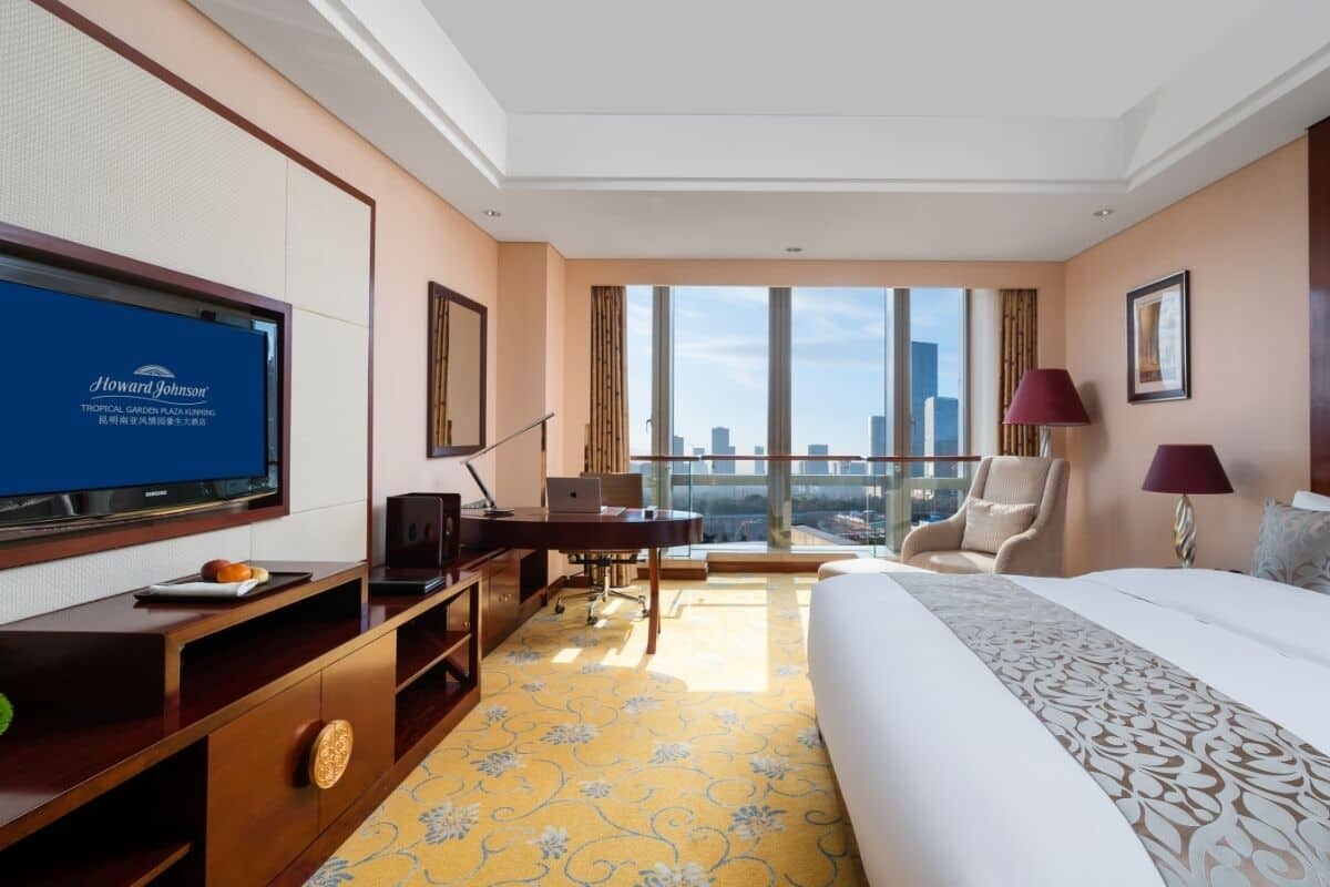 Ein Hotelzimmer mit einem großen Bett, einem Schreibtisch, einem Fernseher und Blick auf die Stadt.