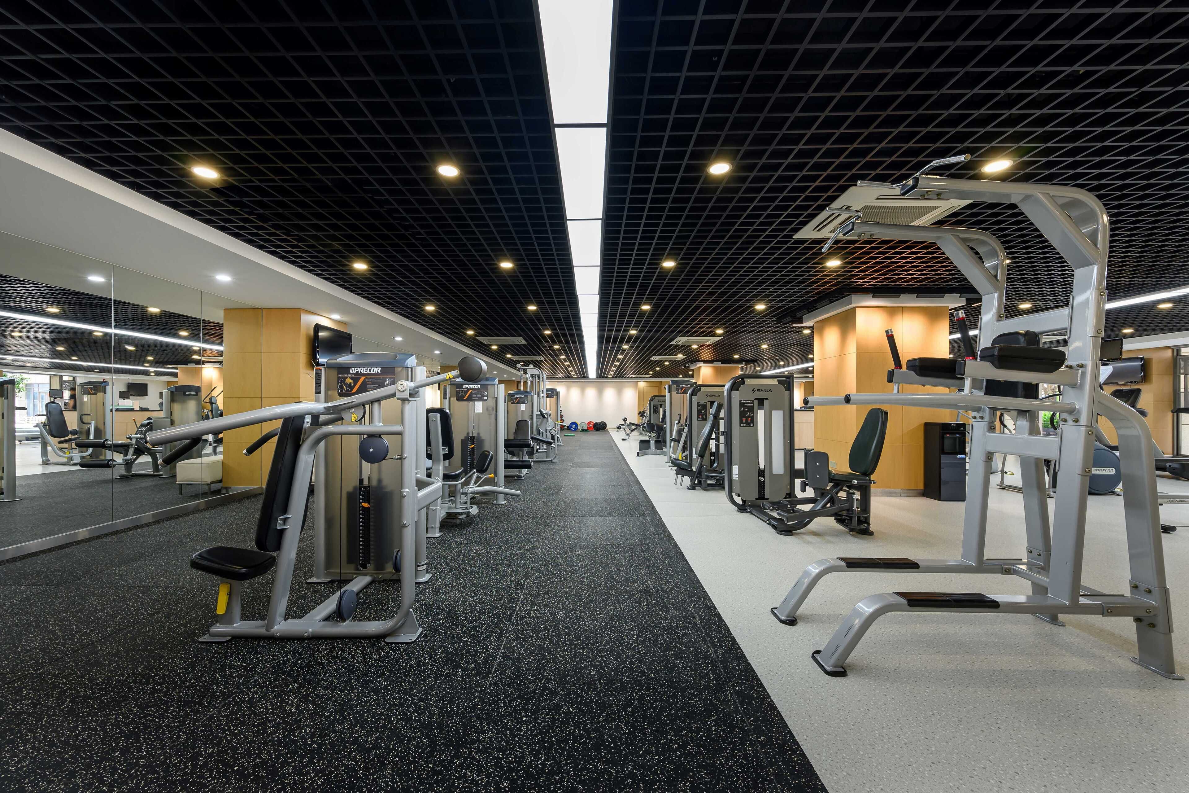 A modern gym with various exercise machines, a mirrored wall, and a black and white floor.