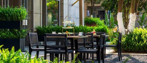 An outdoor seating area with tables and chairs, surrounded by lush greenery and plants.