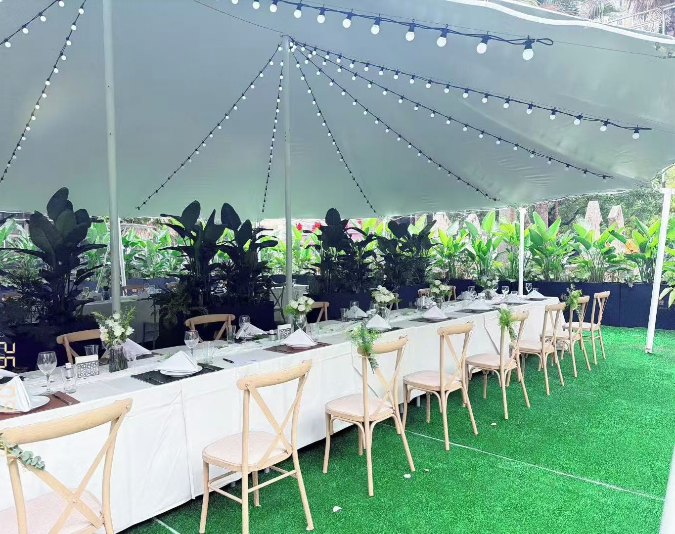 A tented outdoor dining area with tables set for a meal, surrounded by chairs and greenery.