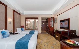 Habitación de hotel con dos camas, televisión, escritorio con frutero y baño visible a través de una puerta abierta.