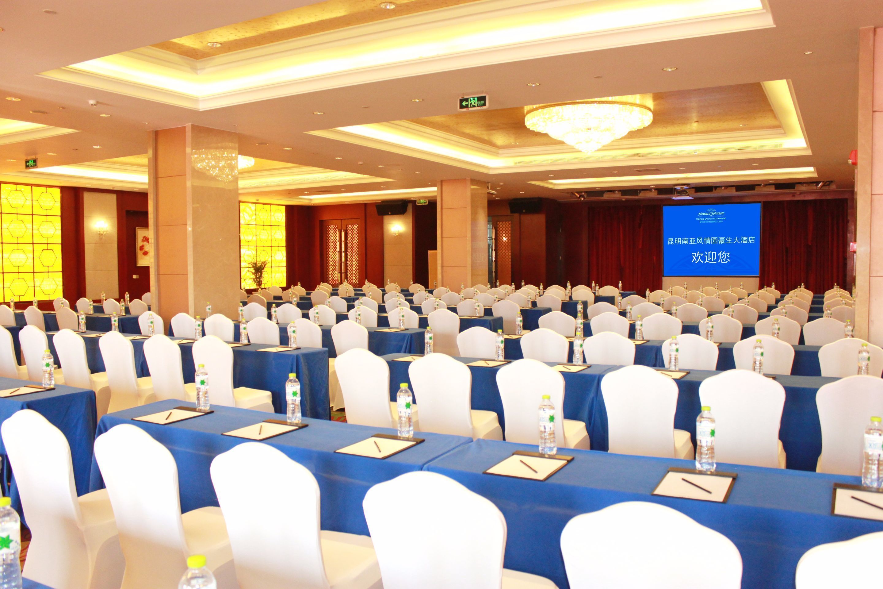 A conference room with rows of tables, white chairs, and a large screen displaying text.