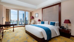 Quarto de hotel com uma cama grande, uma escrivaninha e vista para o horizonte da cidade.