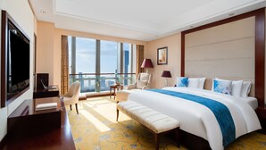 Quarto de hotel com uma cama grande, uma escrivaninha com um laptop, uma cadeira, uma televisão e varanda com vista para a cidade.