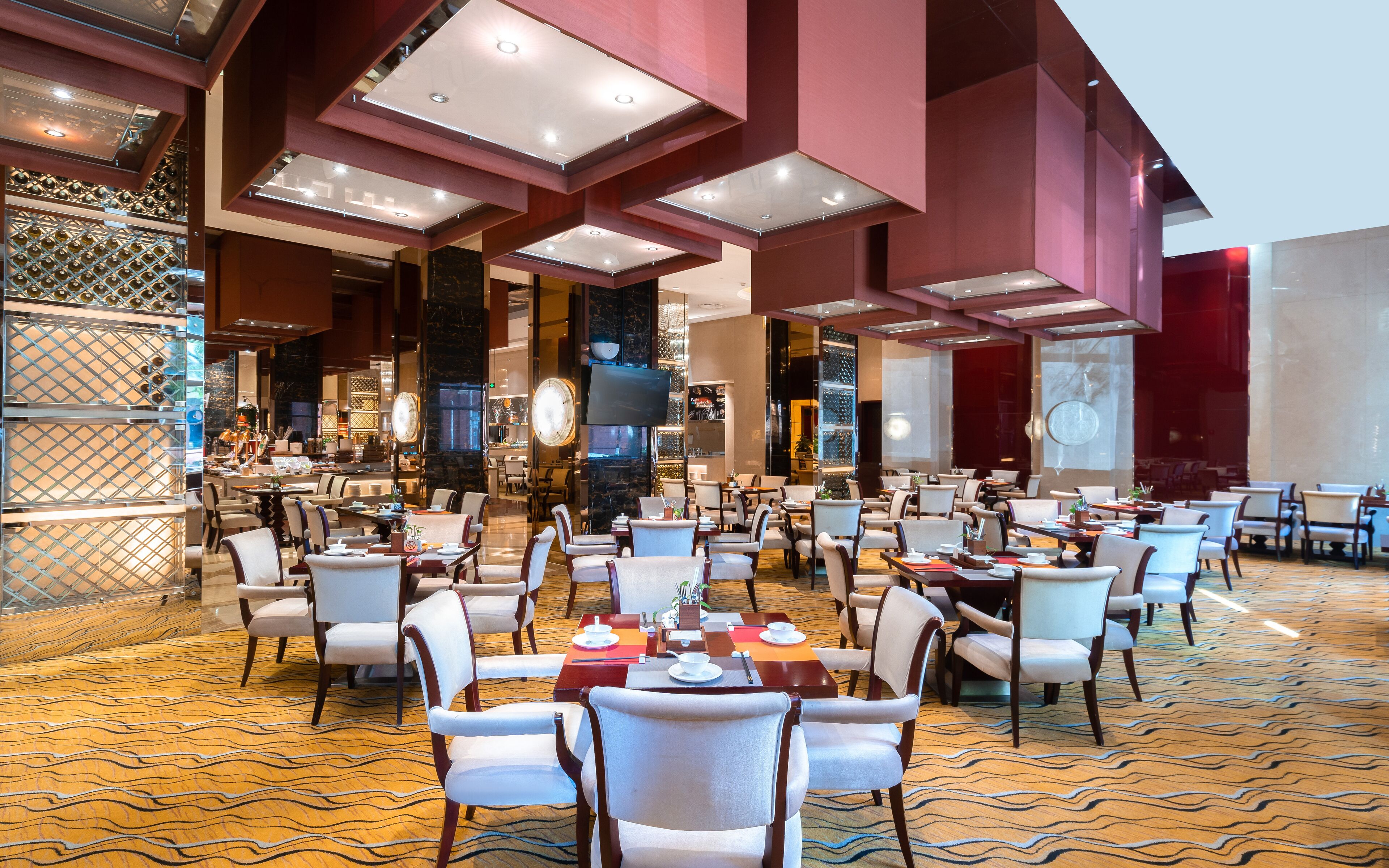 A spacious dining area with multiple tables and chairs, a large screen, and a patterned carpet.