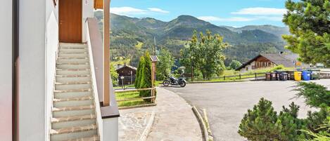 Un edificio con una escalera que lleva a una puerta de madera, un área pavimentada y una vista de montañas al fondo.