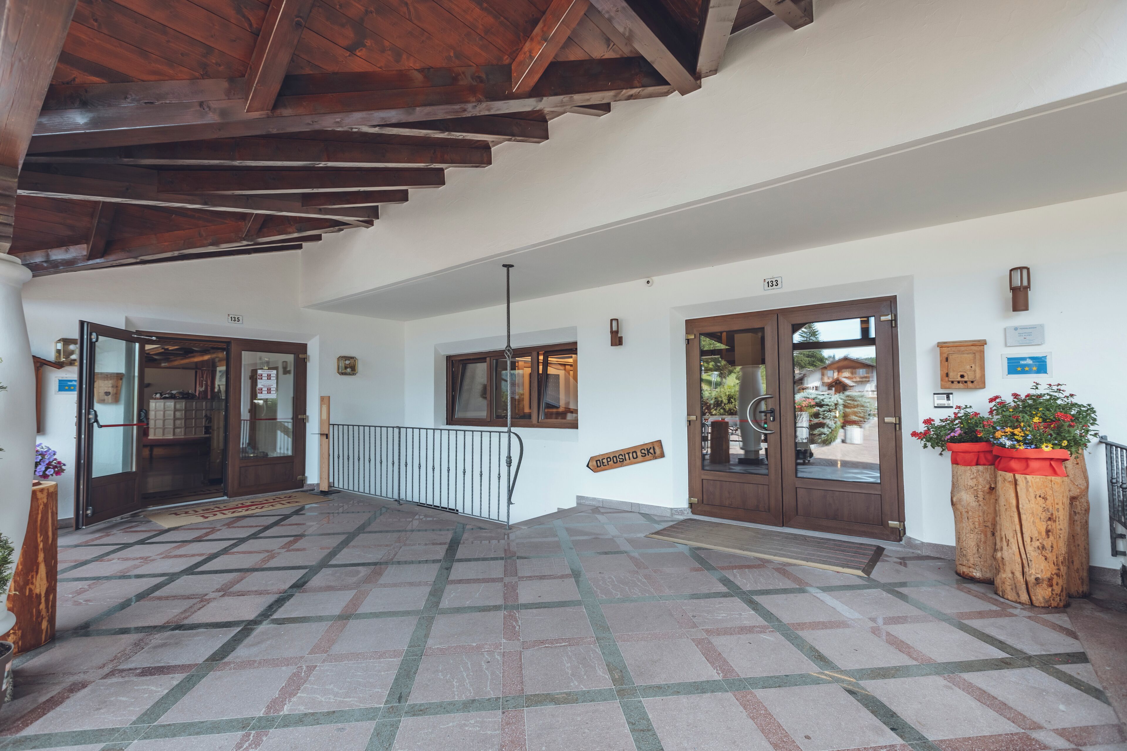 A spacious lobby with a tiled floor, wooden ceiling beams, and a sign indicating a ski deposit.