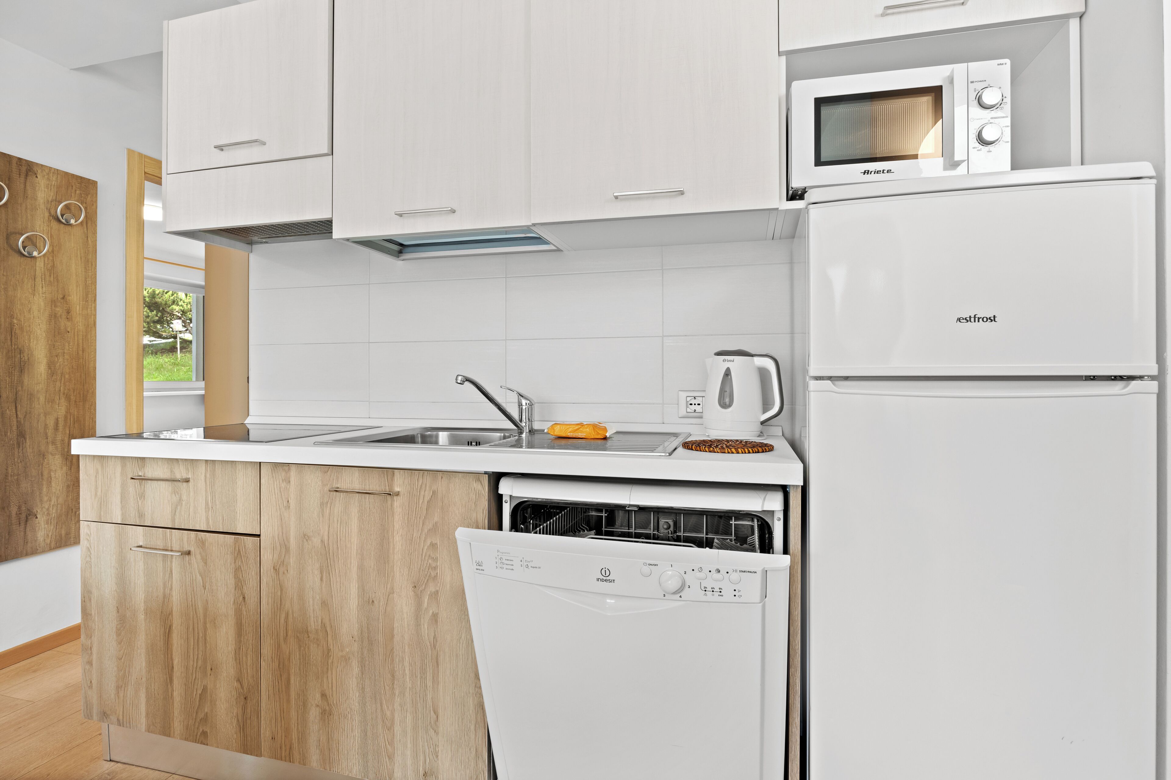 Una cocina moderna con armarios blancos, lavavajillas integrado, refrigerador y microondas.