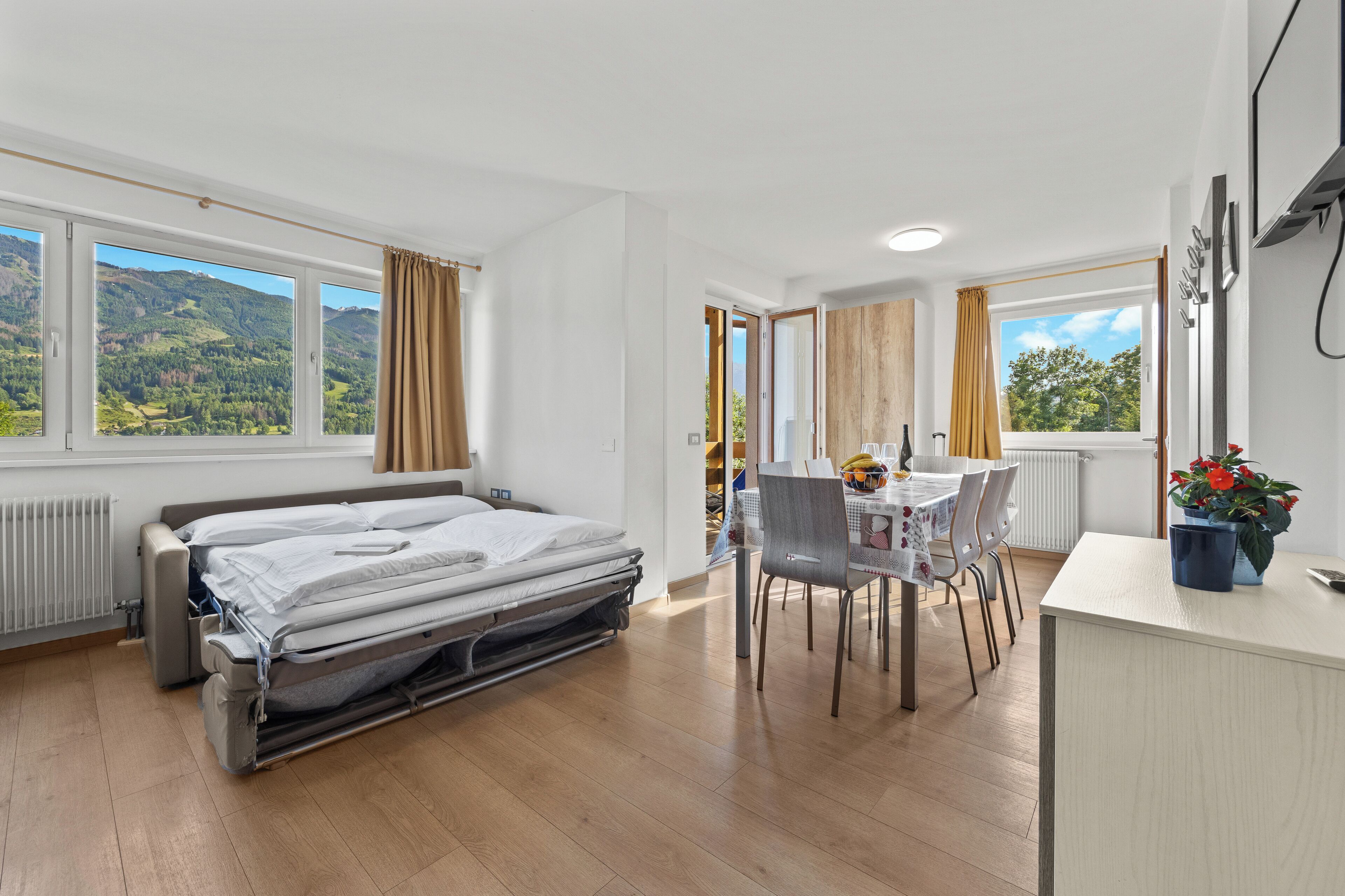 A modern hotel room with a bed, a dining area, and large windows offering a mountain view.