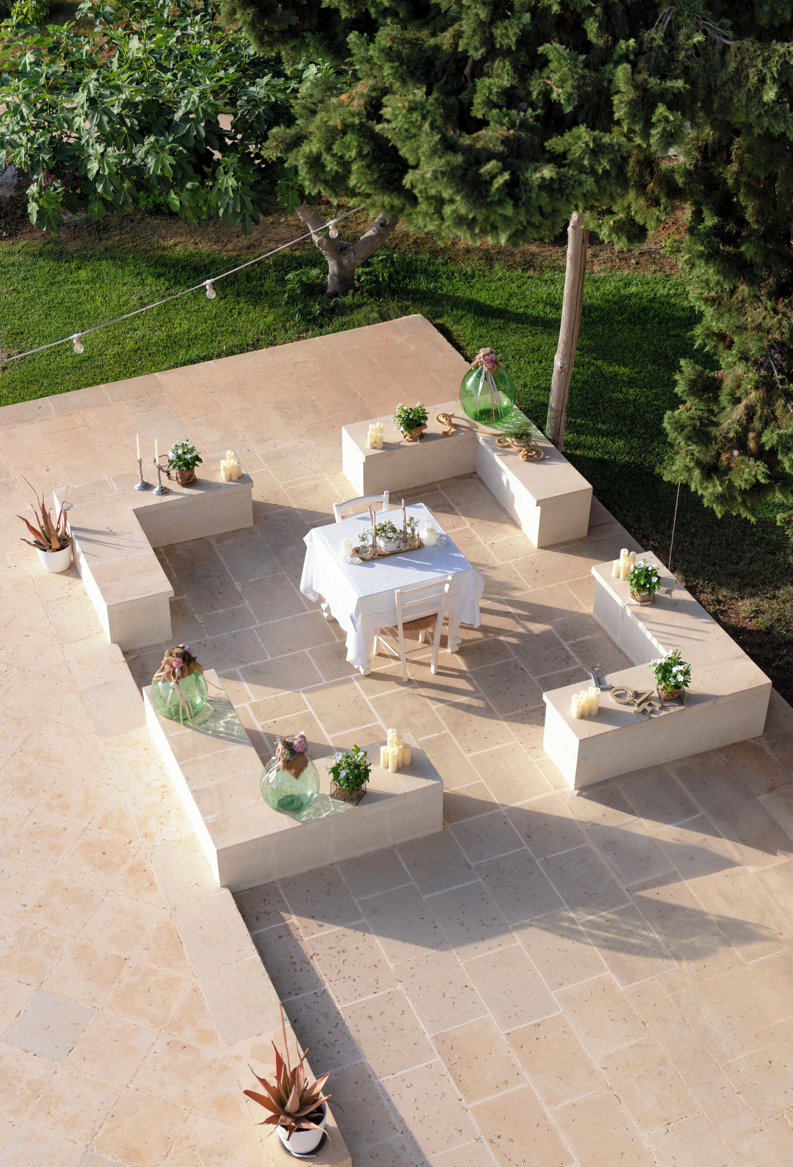 An outdoor patio with a central table surrounded by seating areas, each with potted plants.