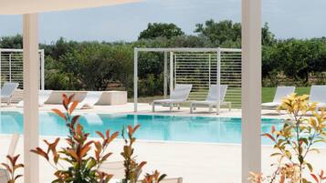 Uma área de piscina com espreguiçadeiras brancas e uma estrutura de pérgola.