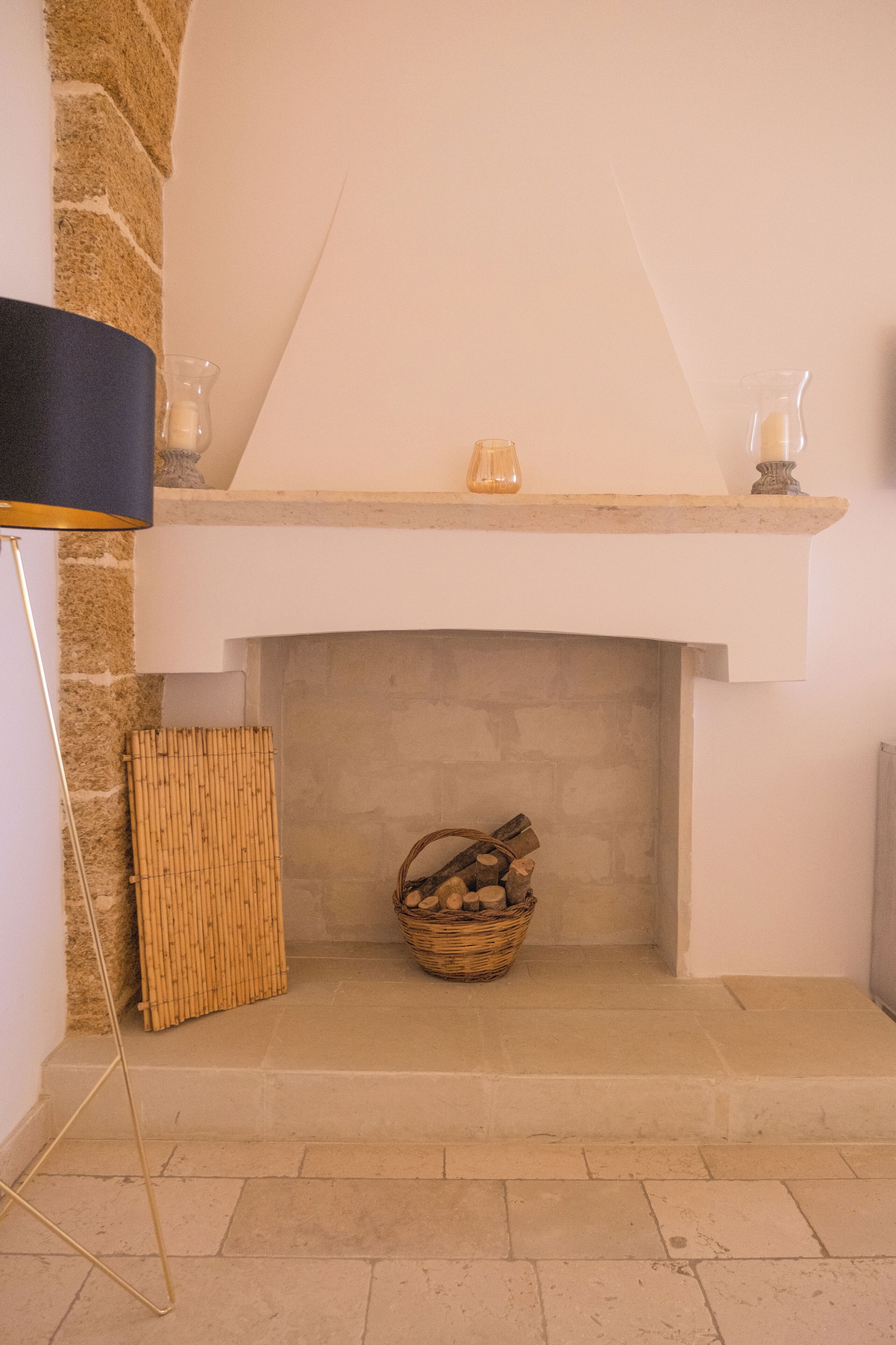 Une cheminée avec un manteau en pierre, un panier de bois de chauffage et une lampe.