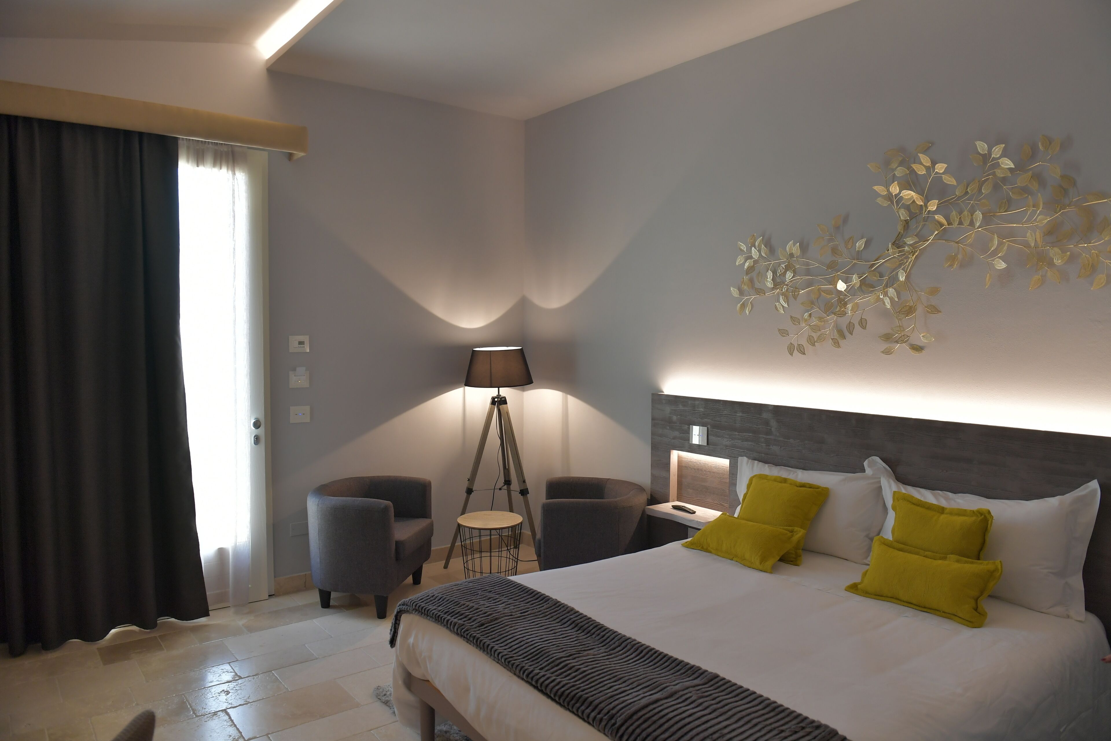 A modern hotel room with a large bed, a desk, and two armchairs.