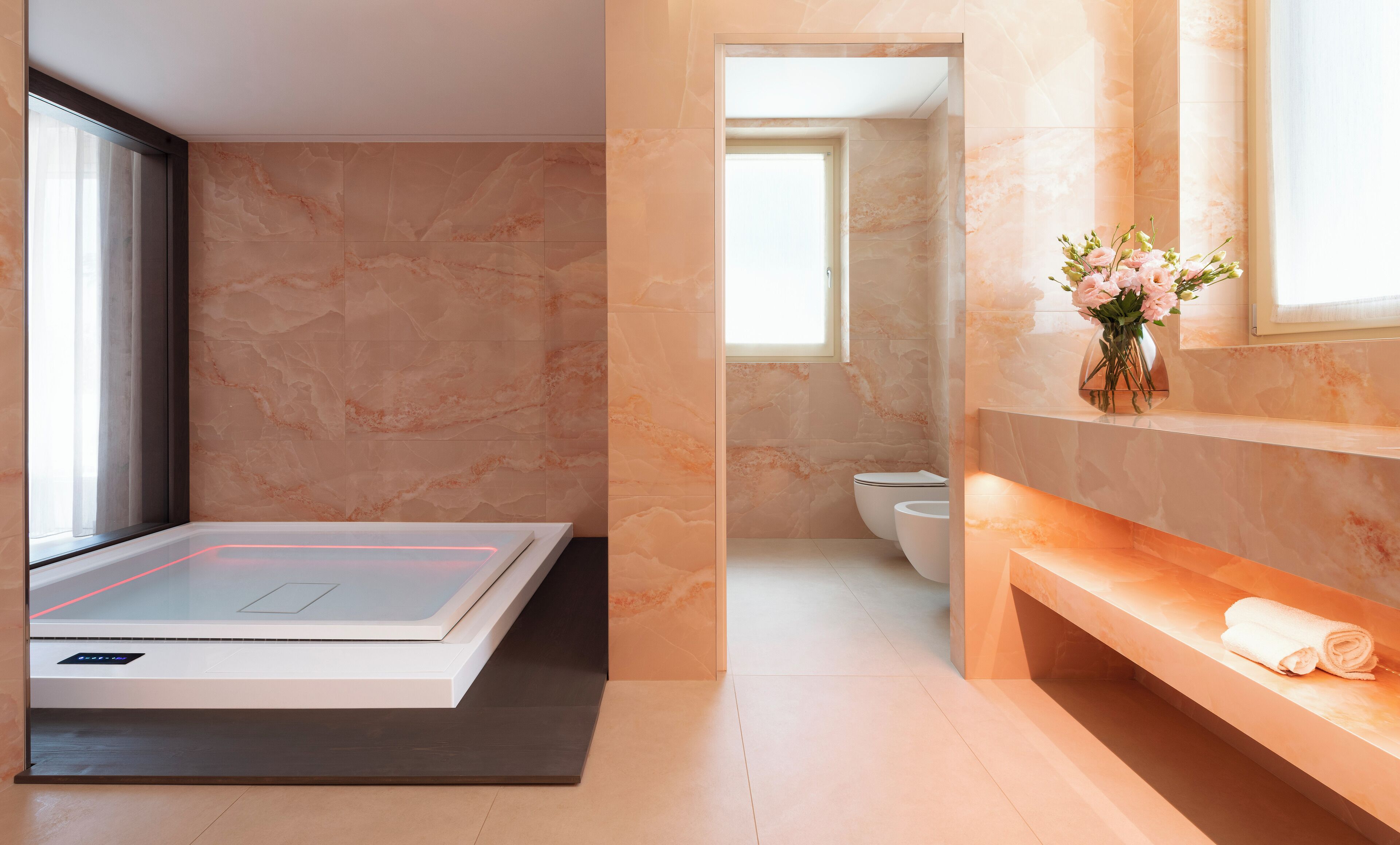 Un baño moderno con una bañera hidromasaje de vidrio, inodoro empotrado y tocador con toalla.