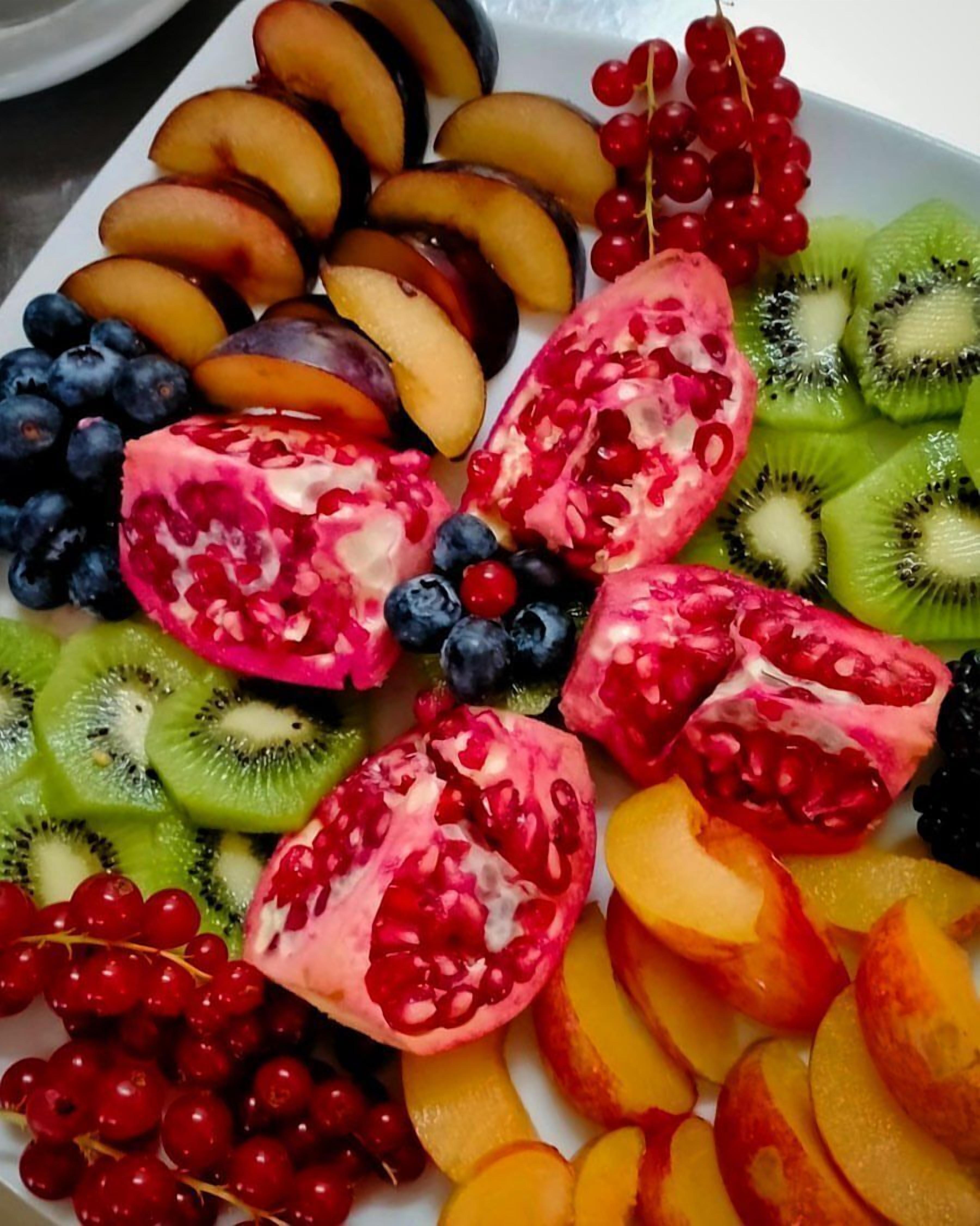 A fruit platter with sliced peaches, blueberries, pomegranate, kiwi, and red currants.