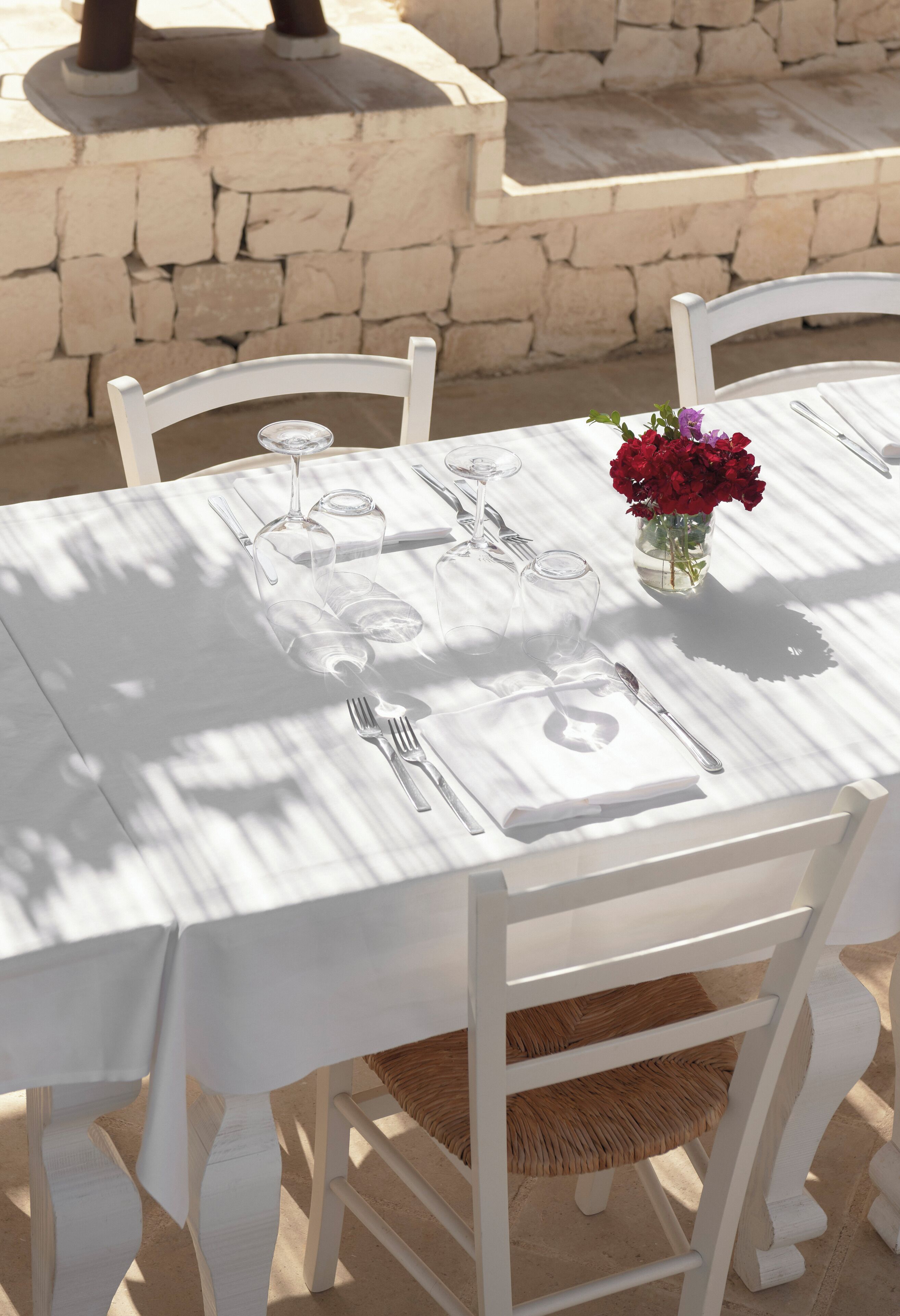 Une table dressée pour le repas, avec une nappe blanche, des chaises et un vase rempli de fleurs.