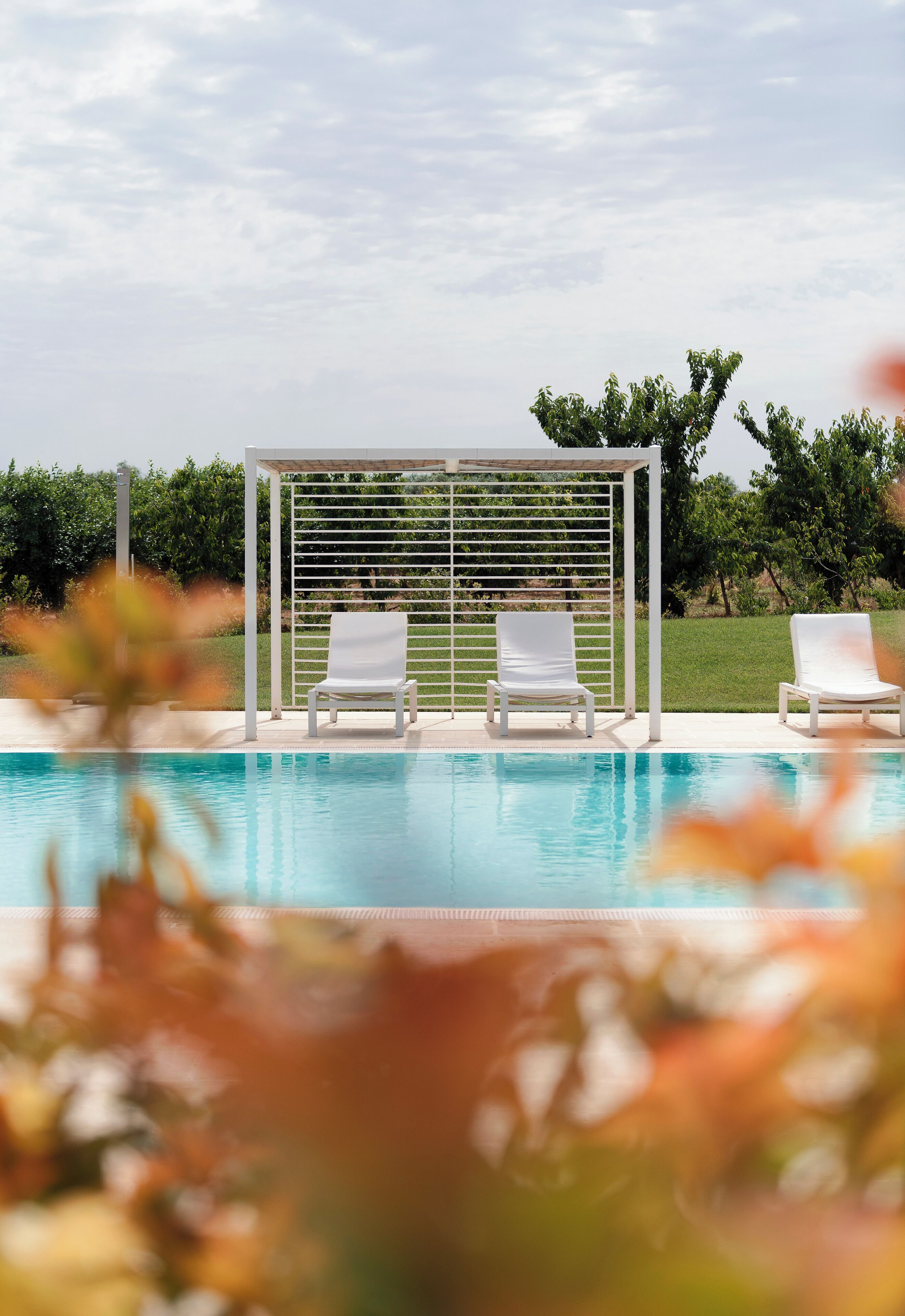 A pool area with two white lounge chairs and a pergola structure.