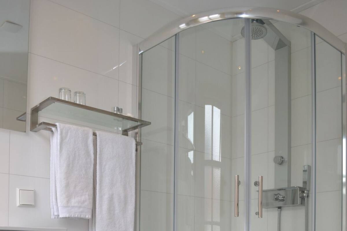 A modern bathroom with a glass-enclosed shower, white tiles, and a white toilet.