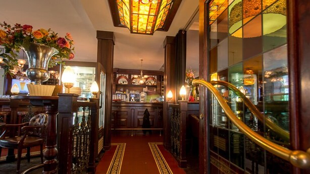 A hotel lobby with a central staircase, a bar area, and a decorative stained glass ceiling.