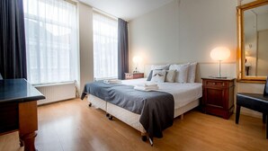 A neatly arranged bedroom with a bed, bedside tables, a desk, and a chair.