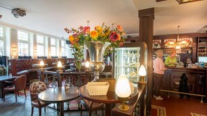 A restaurant with wooden tables and chairs, a large vase with flowers, and a bar area.