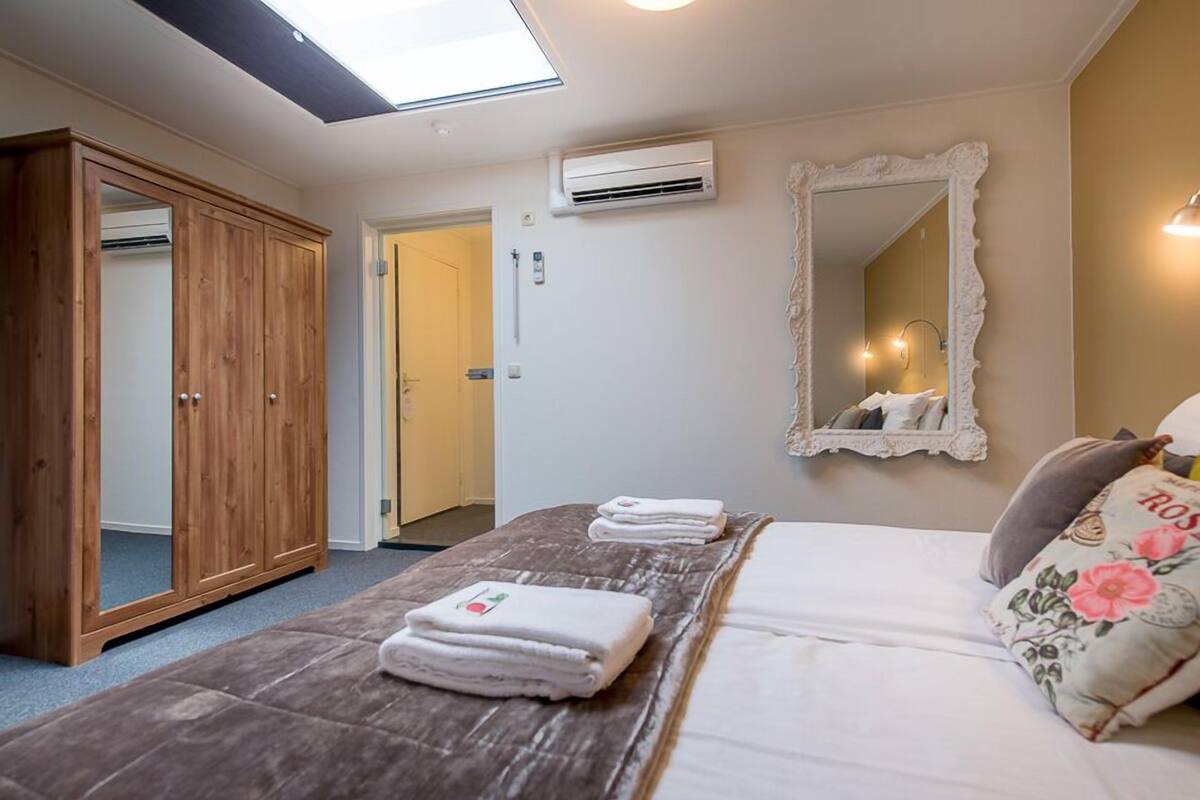 A bedroom with a bed, a wooden wardrobe, an air conditioning unit, and a mirror on the wall.