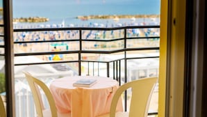 A balcony with a table and chairs, overlooking a beach with umbrellas and boats. - Hotel Royal (Cattolica)