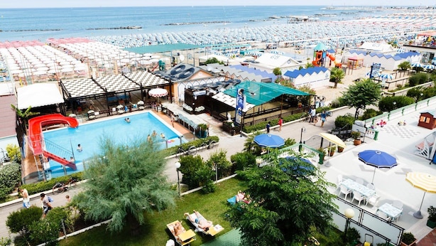 A resort with a large pool, multiple beach umbrellas, and a water slide. - Hotel Royal (Cattolica)