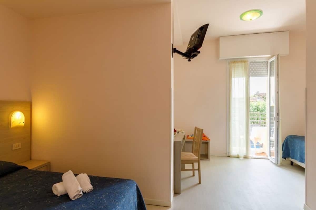 A hotel room with a bed, a desk, and a chair. There is a window with a view of the outside.
