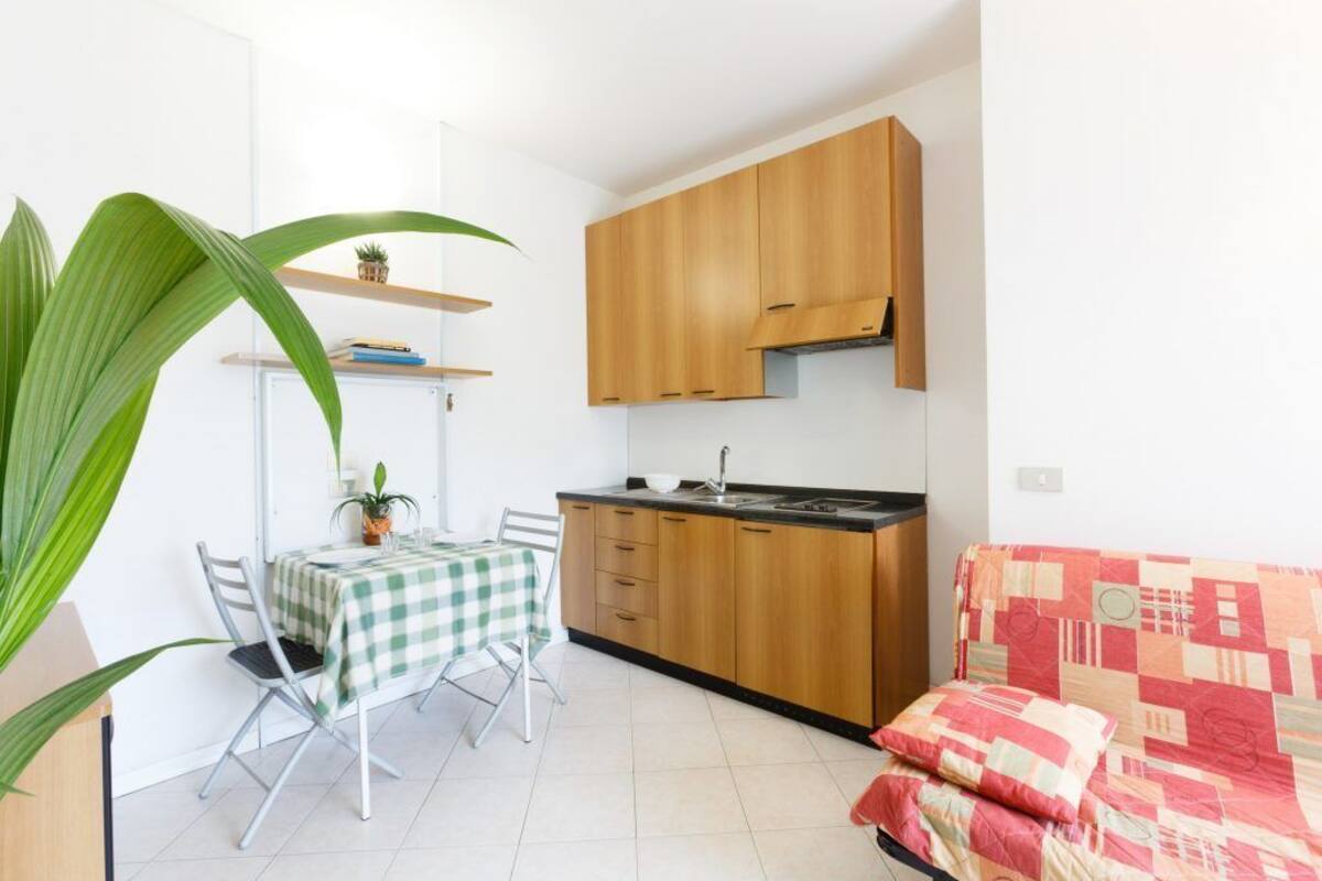 A compact kitchen with wooden cabinets, a dining table with chairs, and a sofa.