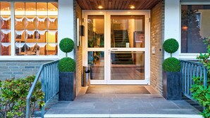 A modern building entrance with a glass door, a wooden ceiling, and two potted topiary plants. - Hotel Stadt Grevenbroich (Grevenbroich)