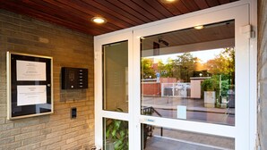 A glass door entrance with a keypad lock, a framed notice, and a potted plant. - Hotel Stadt Grevenbroich (Grevenbroich)