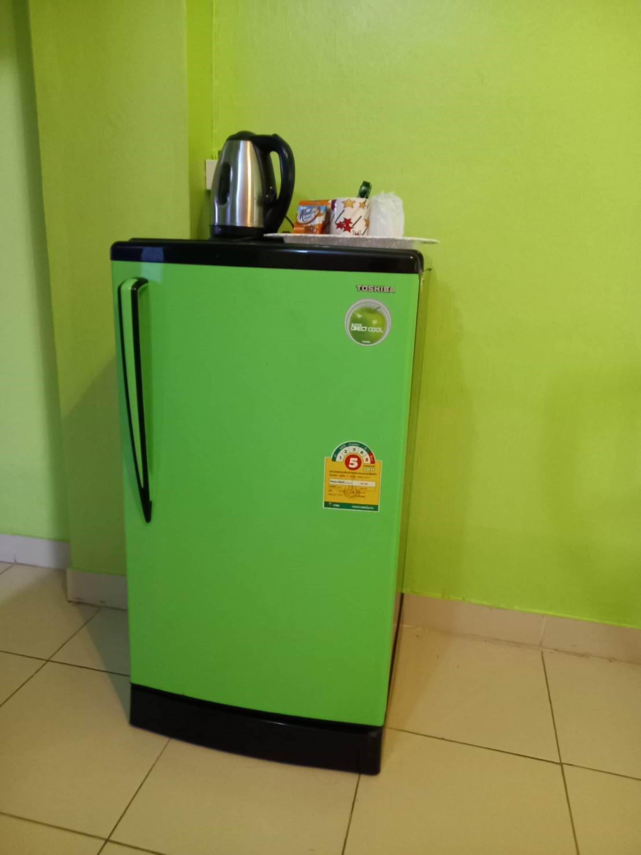 Een groene koelkast met een zwarte handgreep, een roestvrijstalen waterkoker erboven en een sticker waarop staat dat het een Toshiba model is.