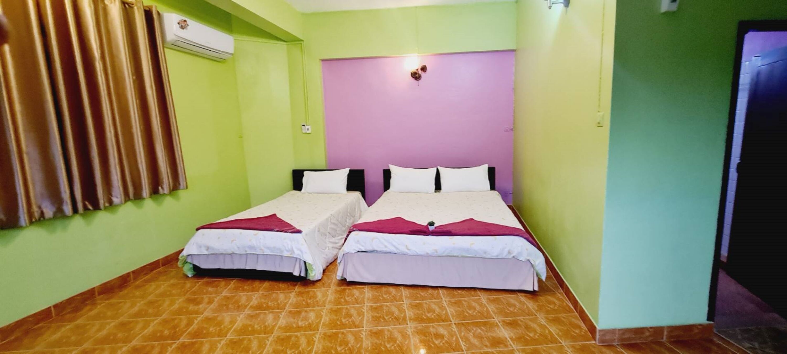 A room with two beds, green walls, a purple headboard, and a tiled floor.