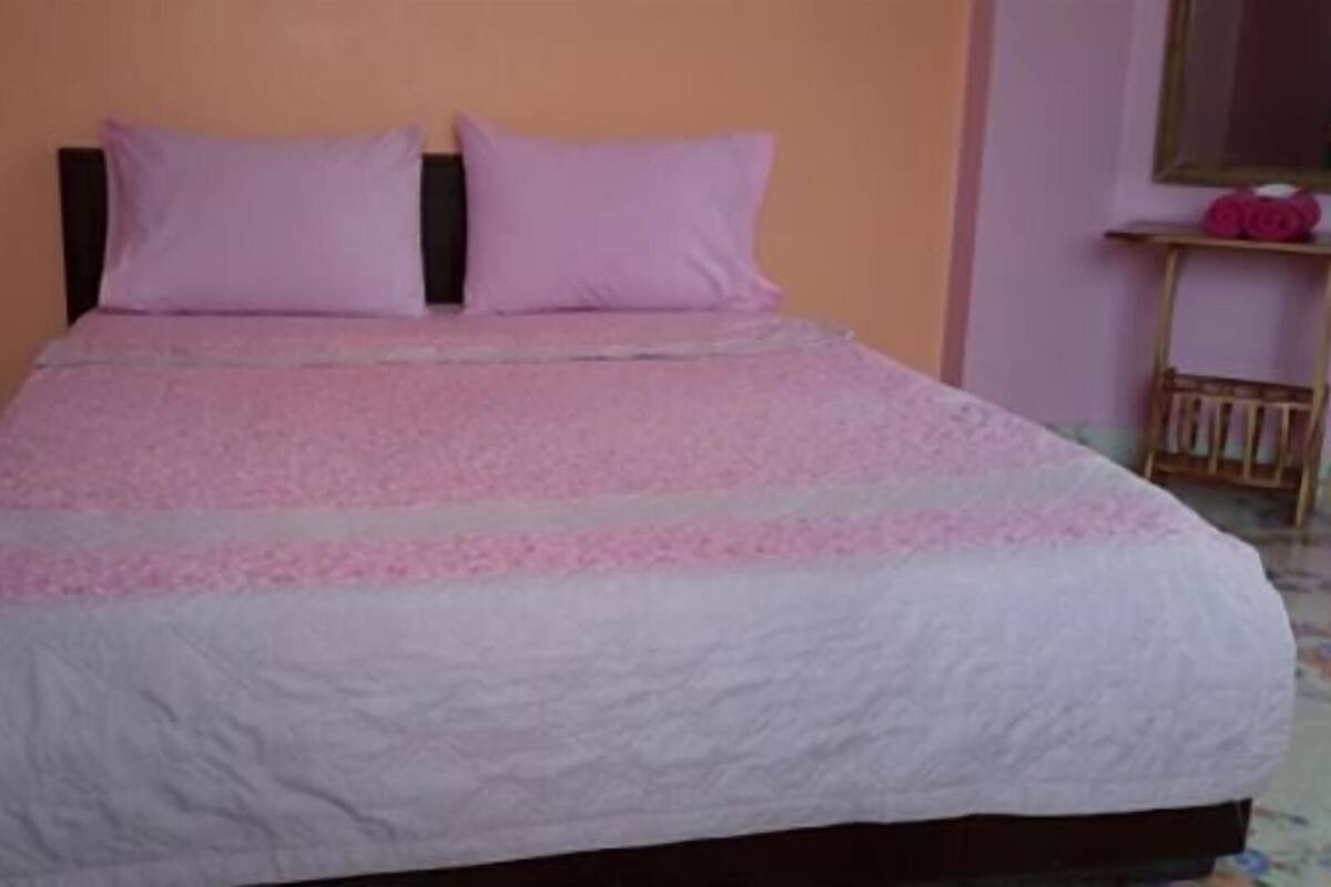 A bed with a pink and white bedspread, a wooden headboard, and a small wooden nightstand with a mirror and pink items.